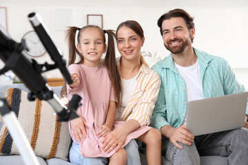 Fototapeta premium Little girl with her parents and telescope using laptop at home