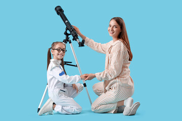 Fototapeta premium Little girl in astronaut costume with her mother and telescope on blue background
