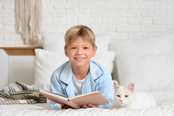 Naklejka premium Cute little boy with cat reading book in bedroom