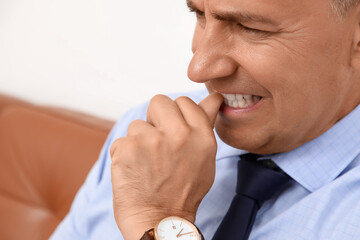 Worried mature businessman biting nails in office, closeup
