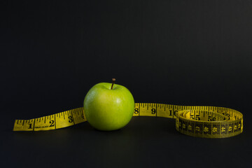 Green apple with yellow measuring tape on dark background for diet concept
