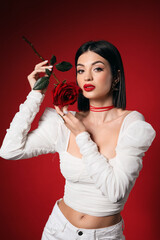 Beautiful young elegant woman with rose on red background