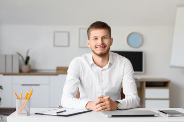 Obraz premium Handsome young happy businessman with laptop sitting at table in office