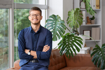 Fototapeta premium Handsome young happy businessman in eyeglasses sitting on sofa at office