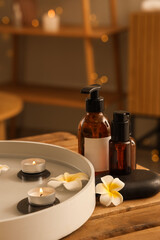 Plate with candles, spa stones, plumeria flowers and cosmetic products on table in salon