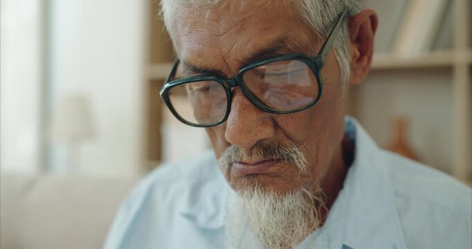 Elderly Asian man with white goatee on sofa in sunlit living room, senior retirement lifestyle and mindful healthy aging in natural light