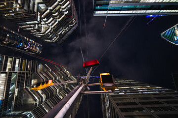 Obraz premium A red traffic signal hangs like a suspended ember between towering glass facades, while cables radiate from the pole like the strings of a giant urban instrument.