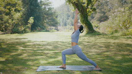Asian woman practicing yoga outdoors in park under soft sunlight, focused balance posture with calm...