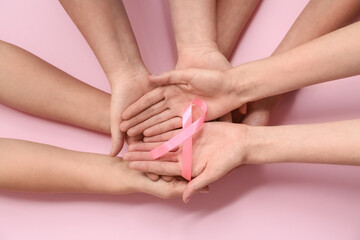 Fototapeta premium Hands holding pink ribbon on pink background, breast cancer awareness support, solidarity and prevention campaign concept