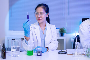 Fototapeta premium Asian woman scientist researcher holding test tube and looking at liquid while working in lab room.