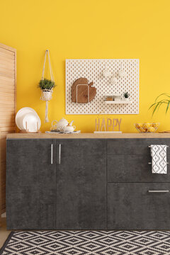 Interior of stylish kitchen with black counters and peg board near yellow wall