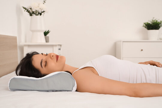 Young woman in pajamas with orthopedic pillow sleeping on cozy bed at home