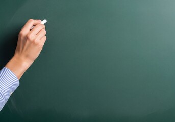 Hand holding white chalk poised to write on a clean dark green chalkboard with ample copy space, bright studio light.