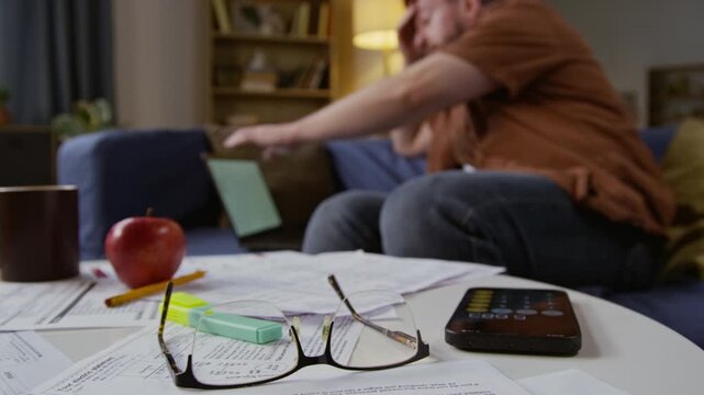 Close up shot of eyeglasses on table over various documents with digital calculator . exhausted man in blurred background, copy space