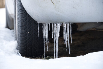 Close-up of icicles hanging from a car bumper in the winter snow