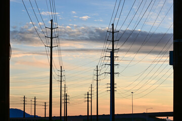 Power transmission lines and utility poles stretching across landscape at sunset, representing electrical infrastructure, energy distribution, and power grid network © Eduardo Barraza