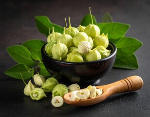 A small black bowl filled with green flower buds next to a wooden spoon and leaves on a dark surface