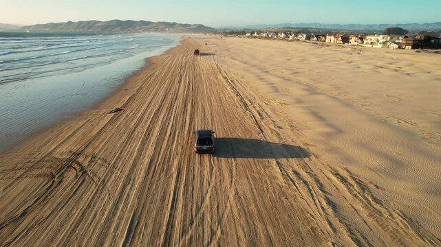 Aerial of van driving on the beach at sunset at Pismo Beach, California