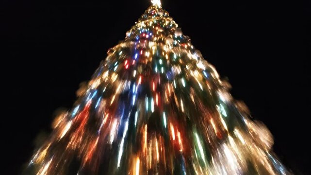 Stylized vertical high-angle shot descending rapidly along the illuminated conical structure of a decorated evergreen tree fading into absolute darkness vertical, mood, verticalpan