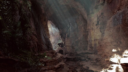 Sunlit cave opening with mossy floor and shallow pools, explorer footprints leading toward bright entrance, rugged rock walls, soft dripping echoes, tranquil