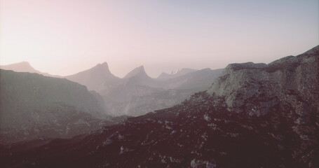 Obraz premium The landscape features rugged mountains bathed in soft morning light, creating a serene atmosphere. The peaks rise majestically, capturing the beauty of natures tranquility.