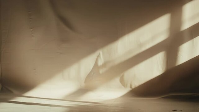 Empty minimalist studio with textured beige fabric draped over wall and floor, warm natural sunlight casting dramatic diagonal shadows for serene product or art presentation