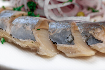 Sliced salted herring fillet with baked potatoes, red onions, and green peas on a white plate, close-up.