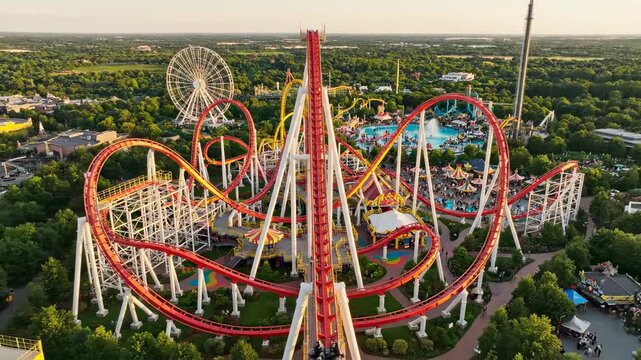 Sweeping drone aerial shot revealing the entire complex track layout of a huge looping roller coaster within a sprawling amusement park landscape perspective, overhead, weekend
