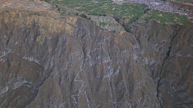 Drone pans across Colca Canyon&rsquo;s mammoth walls, showing the sharp rim drop and contrast between lush terraced farmland above Cabanaconde and the rugged canyon below.