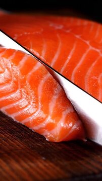Macro close-up shot of a sharp white knife beginning to slice a premium raw salmon fillet resting on a dark wooden cutting board, emphasizing freshnes