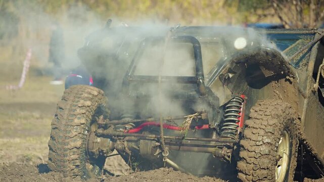 A muddy off-road buggy emits smoke after breaking down in an extreme race. Dynamic video shows detail of the dirty tires and suspension. Intense, powerful motorsports concept. Slow motion