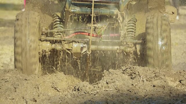 Dynamic action of a rugged off-road vehicle in a race. Close-up, low-angle view of the suspension and wheel churning and splashing thick brown mud. An energetic, extreme sports concept. Slow motion