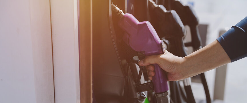 A close-up image of a gas station attendant's hand holding a fuel dispenser.	
