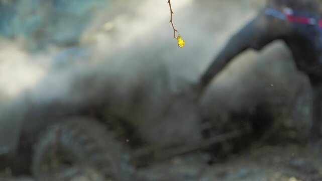 Off-road racing. Selective focus on a yellow leaf contrasts with the blurred motion of an all-terrain vehicle raising a huge cloud of smoke. A powerful, chaotic, and extreme sports concept