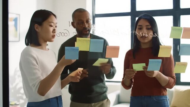 Diverse team collaborates using sticky notes on glass wall.