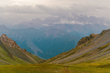 Obraz premium Photo from the back of hikers walking on green grasslands in the Tianshan Mountains in Xinjiang, China. There is snow on the peak with copy space on top. Idea for adventure activity wallpaper.