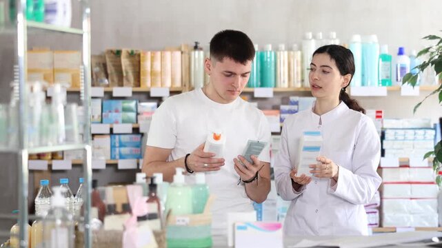 Man chooses skin cream in modern pharmacy. Female pharmacist helps with choosing a medicine. High quality 4k footage