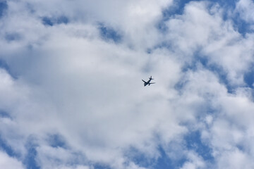 Fototapeta premium A commercial airplane flies high across a bright blue sky filled with soft, white cumulus clouds. Wide-angle view capturing a sense of travel, freedom, and global aviation.