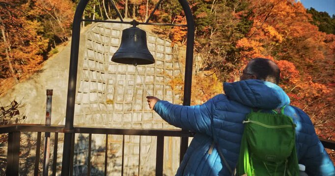 Man ringing beautiful old Japanese bell near ledge - slow motion steady cam shot