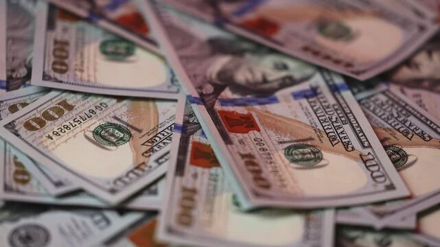 Close-up view of various hundred-dollar bills stacked together, showcasing intricate designs and details of the currency in a well-lit setting