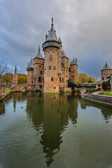 Fototapeta premium Vertical view of De Haar Castle reflecting in the surrounding moat, featuring towers, bridges, and a dramatic sky in Haarzuilens, Netherlands.