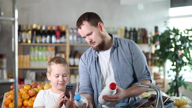 European man with son customer at shop scan QR code on milk bottle using phone camera. Client study composition, manufacturer information of product using application. Visitor examines product