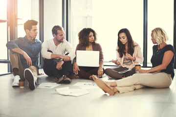 Obraz premium Collaboration, conversation and laptop with designer people on floor of office for planning or research. Computer, design and documents with employee team in creative workplace for project management