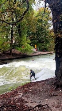Wet suit surfers River Surfing morning Eisbachwelle Eisbach Isar River Munich Germany vertical tourist attraction street view Autumn Fall Englischer Garten standing wave water action sports stunts pan
