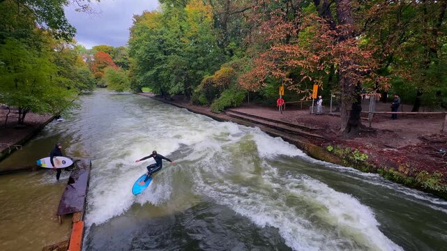 Wet suit surfers River Surfing morning Eisbachwelle Eisbach Isar River Munich Germany tourist attraction bridge view Autumn Fall Englischer Garten standing wave action sports water sports stunts air