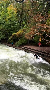 Wet suit surfers River Surfing morning Eisbachwelle Eisbach Isar River Munich Germany vertical tourist attraction bridge view Autumn Fall Englischer Garten standing wave water action sports stunts pan