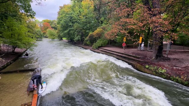 Autumn Fall wet suit surfers River Surfing morning Eisbachwelle Eisbach Isar River Munich Germany bridge view Englischer Garten artificial man made standing wave action sports water sports stunts pan