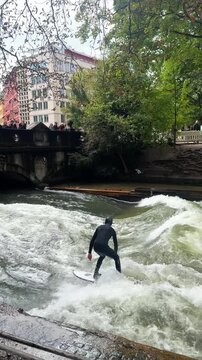 Wet suit surfers River Surfing morning Eisbachwelle Eisbach Isar River Munich Germany vertical tourist attraction bridge view Autumn Fall Englischer Garten standing wave water action sports stunts air