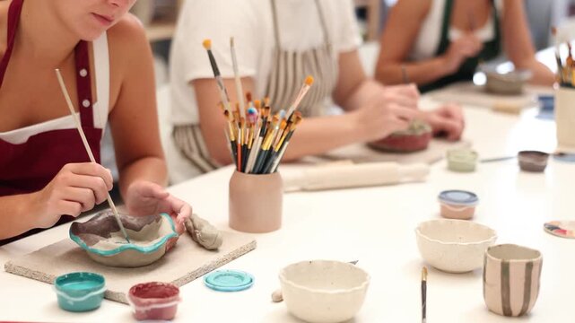 Close up of female hands painting ceramic plate with paint and brush in pottery workshop. High quality 4k footage