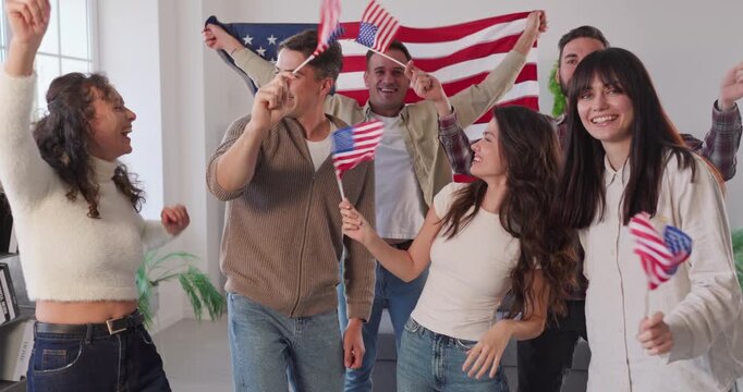USA Independence Day party celebration of young happy people group waving US flags and smiling at home. Cheerful excited friends wave small flags indoors, celebrate patriotic holiday, enjoy unity